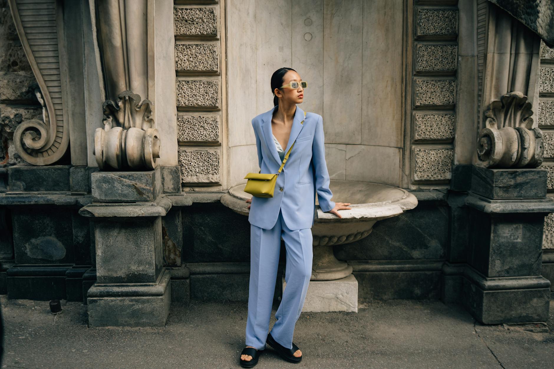 woman in blue suit and green handbag standing beside building