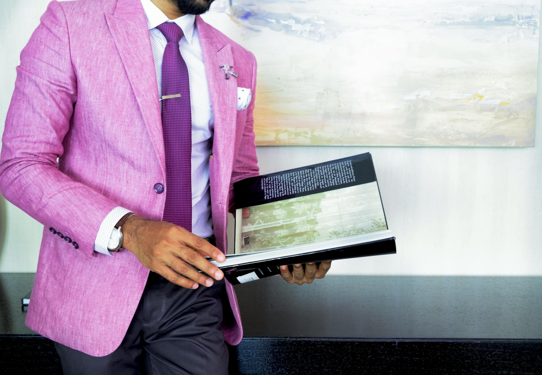 man in pink suit jacket holding book