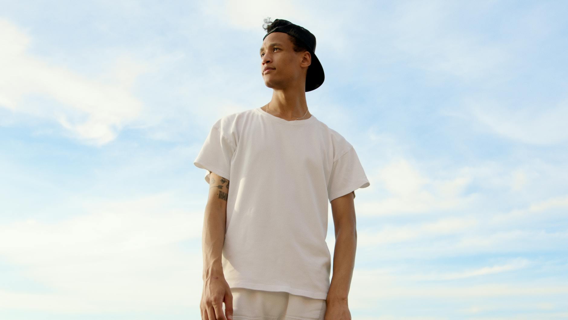 young man in tshirt and cap against white clouds