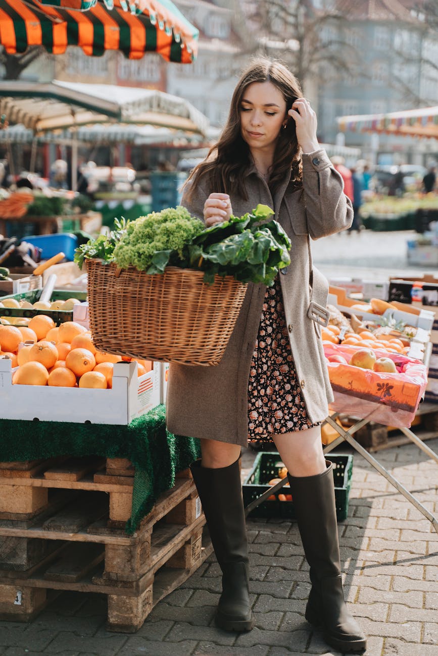 woman in brown coat carrying wicker basket full of green vegetables