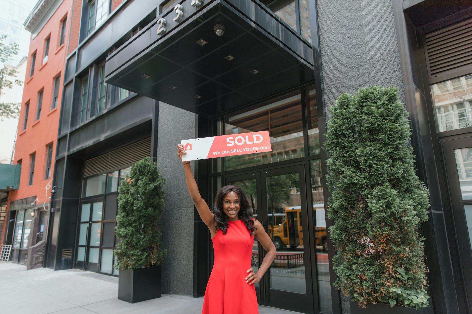woman in red dress holding sold sign above her head