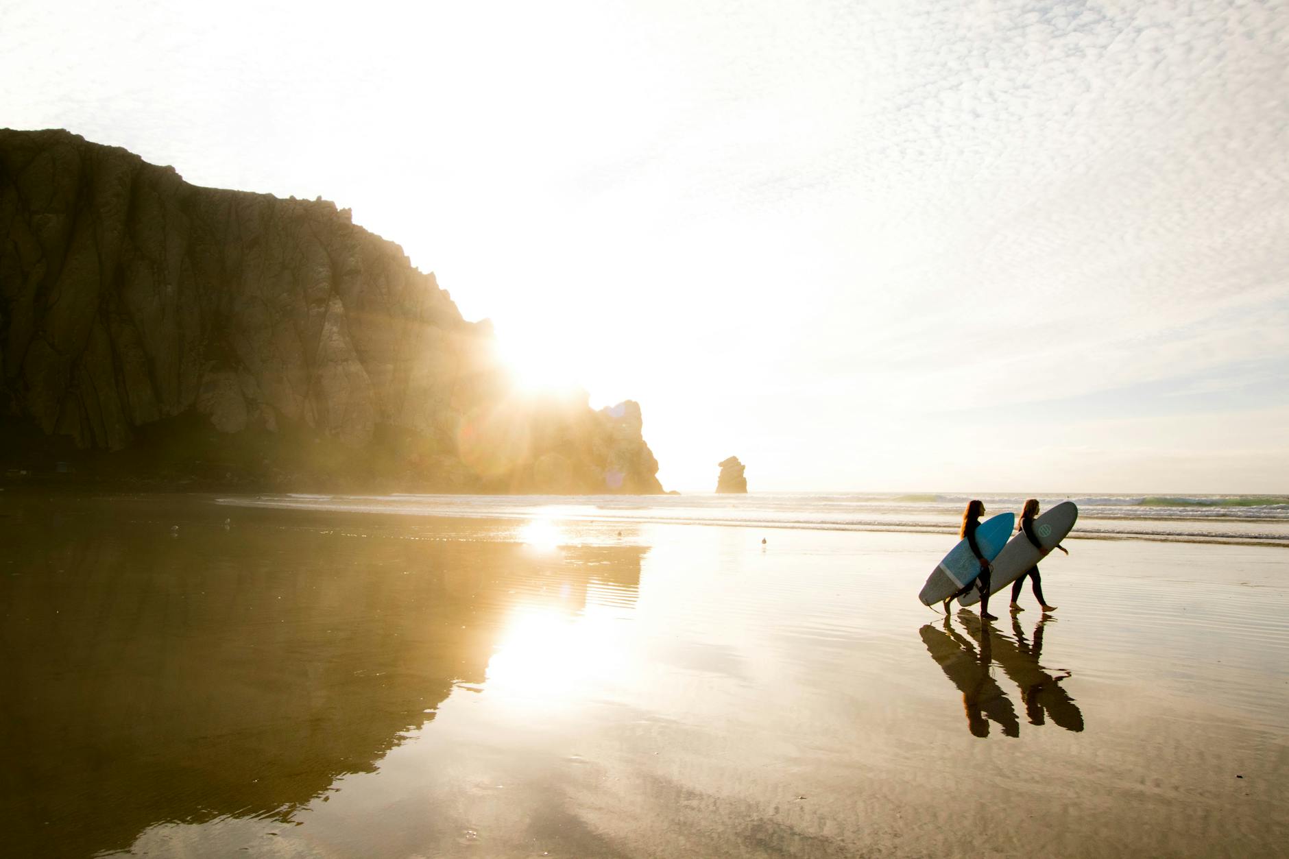 two people carrying surfboards on seashore