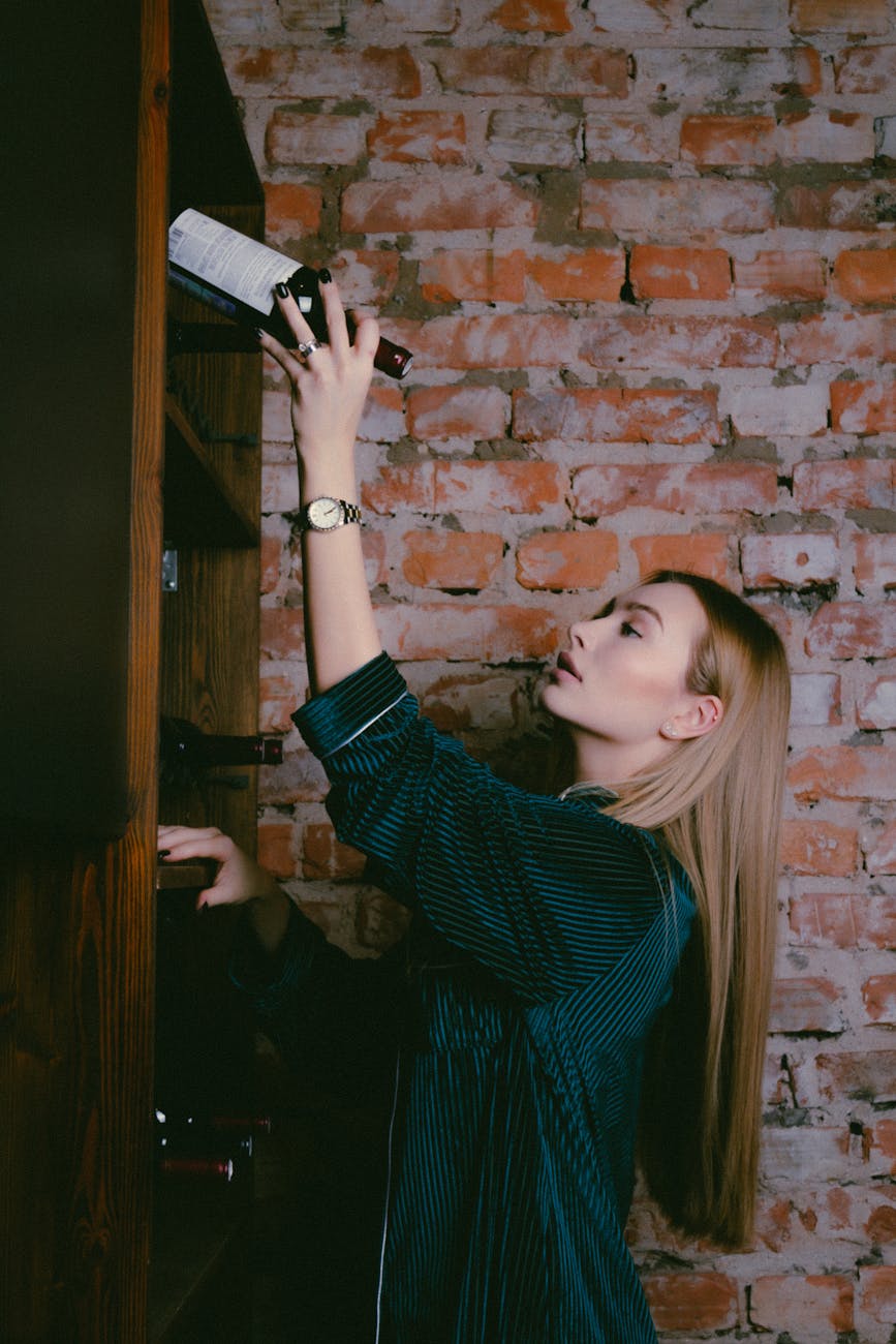 woman in green velvet blouse putting bottle of wine onto shelf in cellar