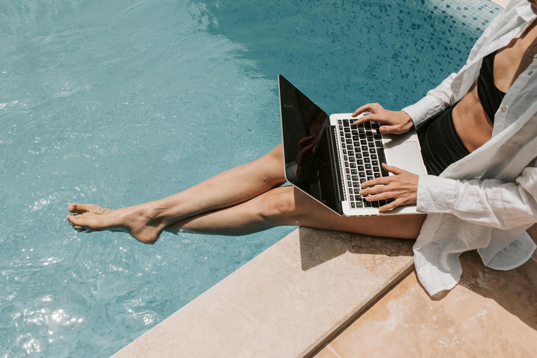 woman sitting on poolside using laptop
