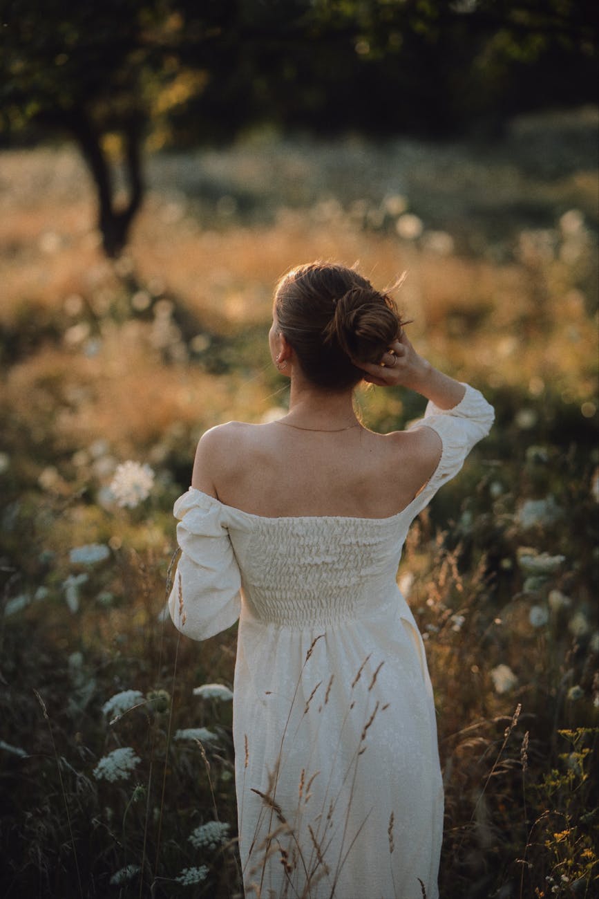 young woman in white off the shoulder dress enjoying the sunrise in the meadow