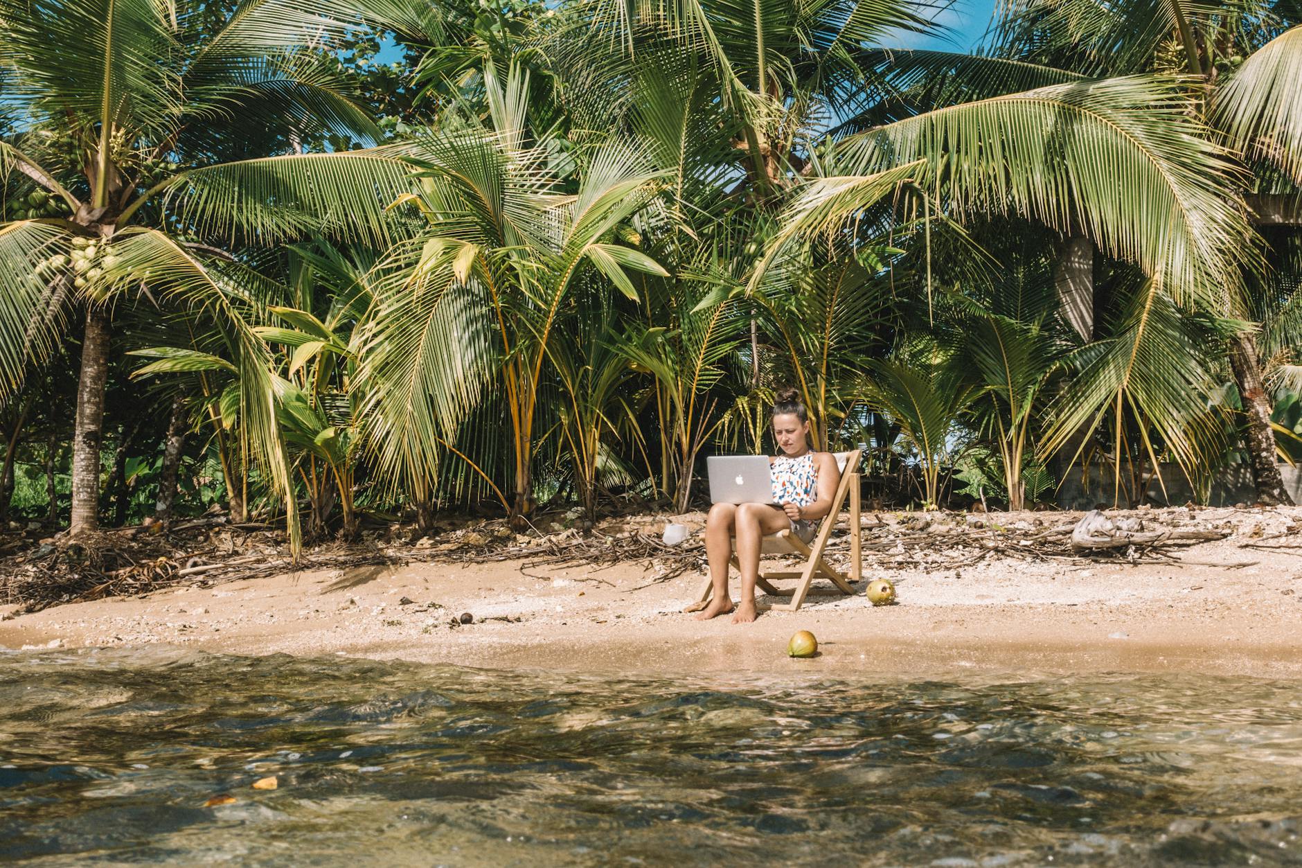 a woman working on the beach while sitting on a wooden chair