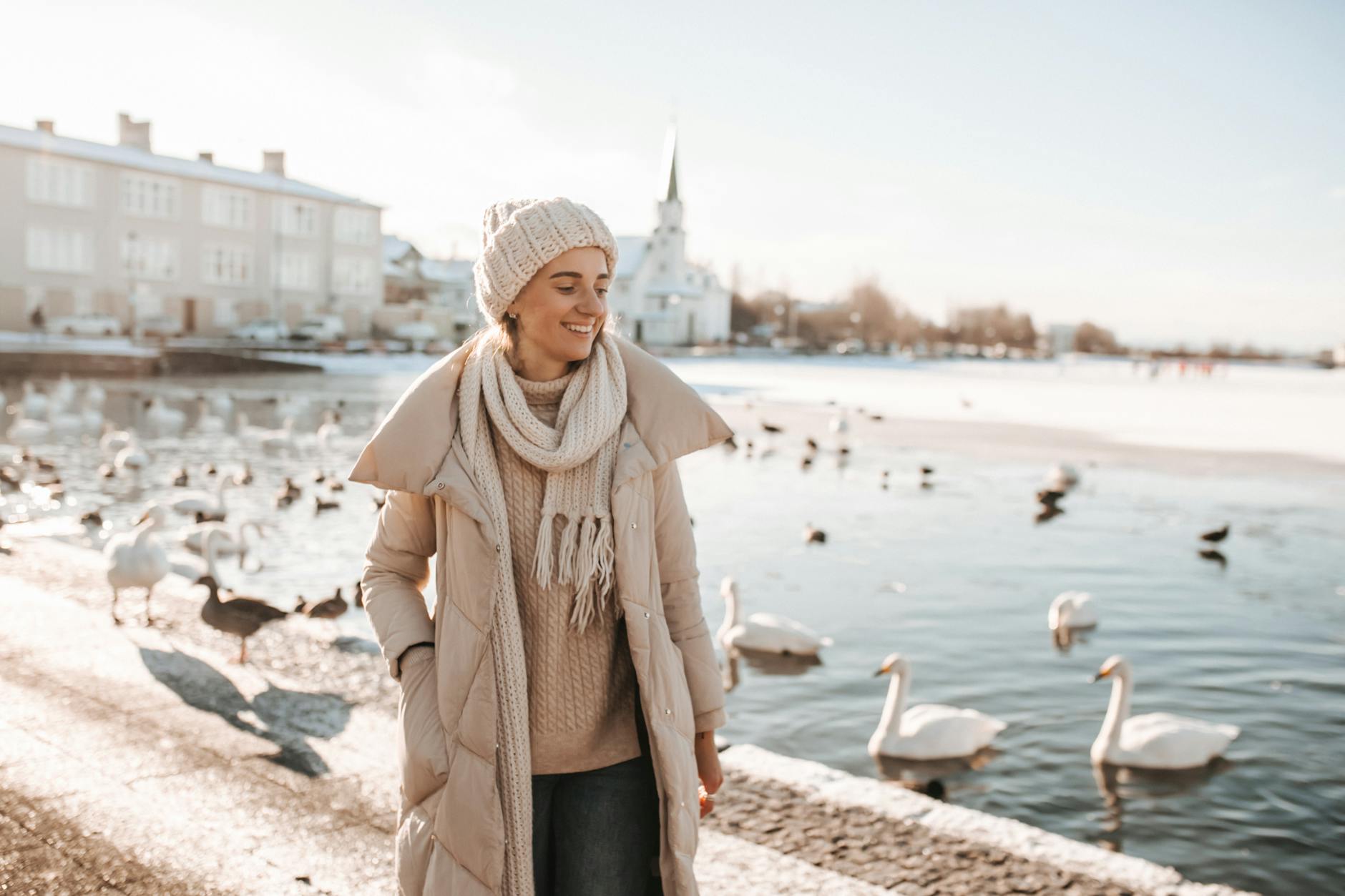 a woman standing near a lake with waterfowls