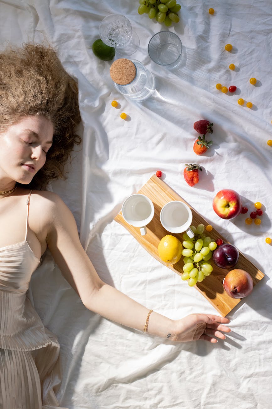 young female with closed eyes lying on blanket near assorted fruits
