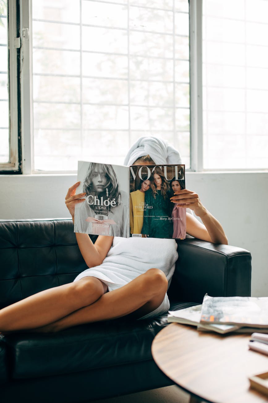 woman reading a vogue magazine while sitting on a couch