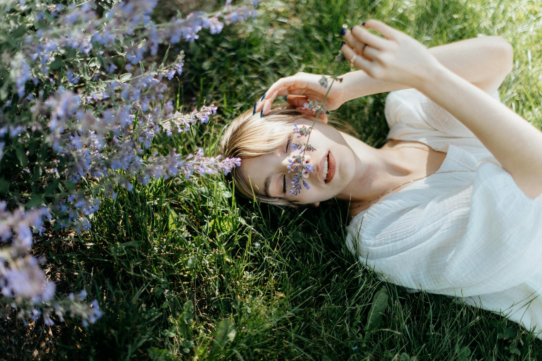 a woman in white top lying on green grass holding a a stem flowers