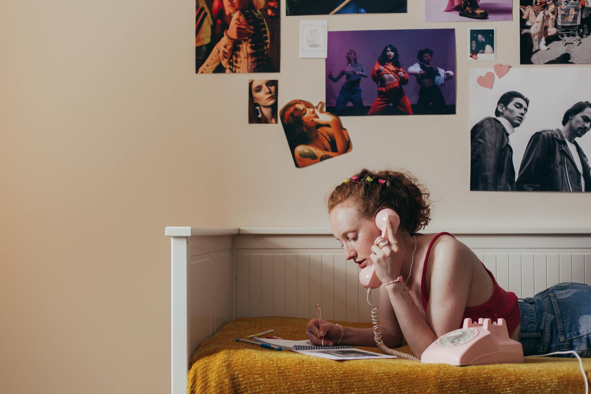 girl writing on notebook while talking on the telephone