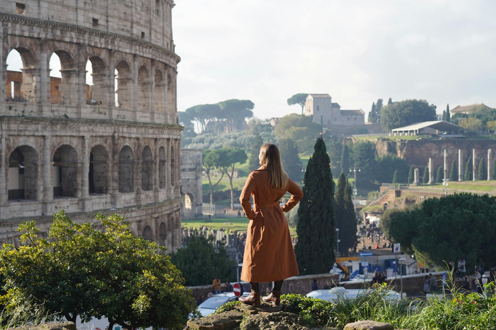 woman in brown coat looking at a ruin