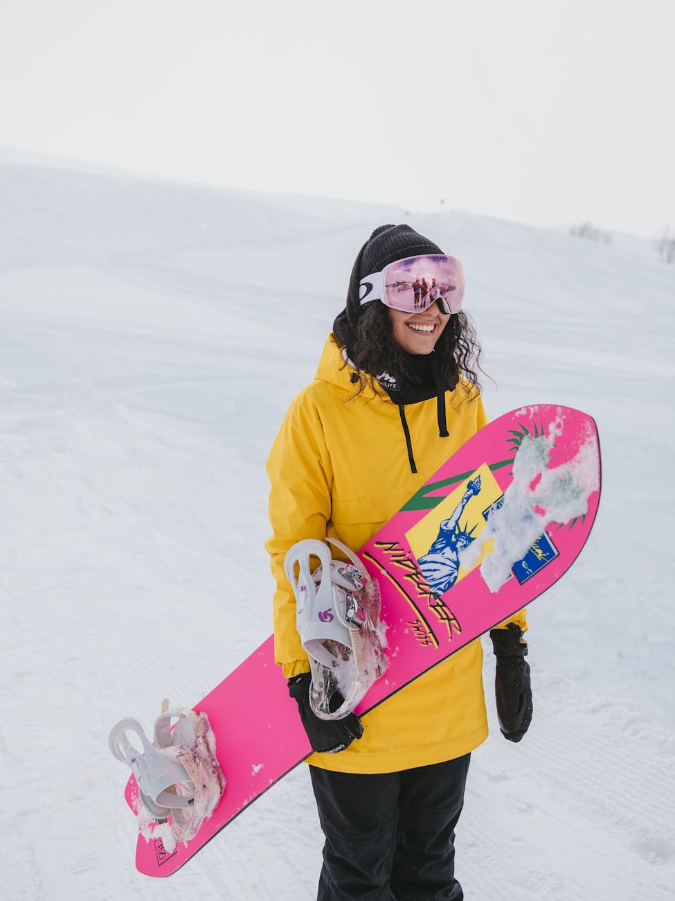 woman in yellow hoodie holding pink and white snowboard