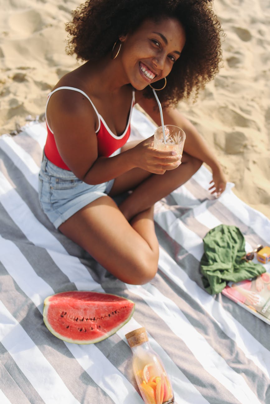 smiling woman sitting on beach towel with a cold drink