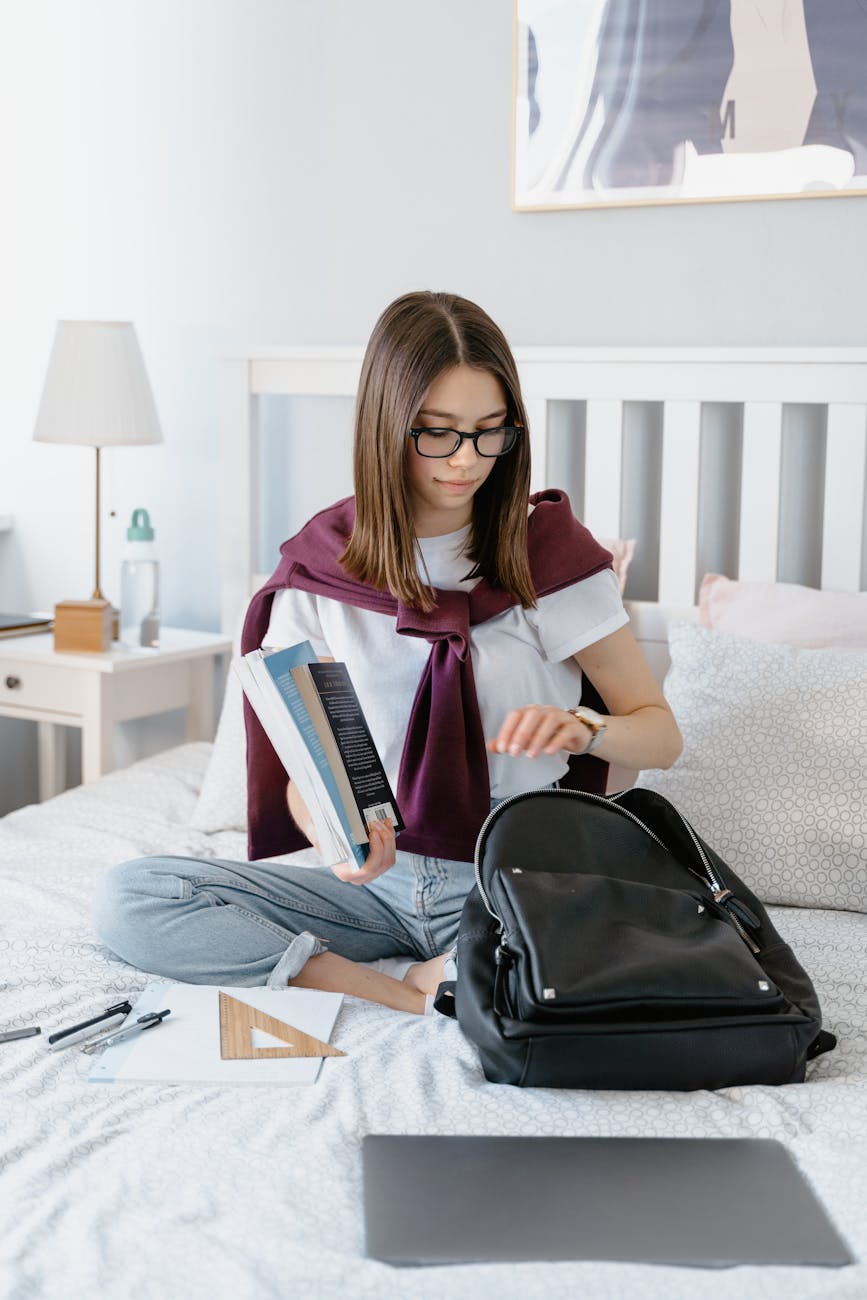 a young woman packing her books while sitting on the bed