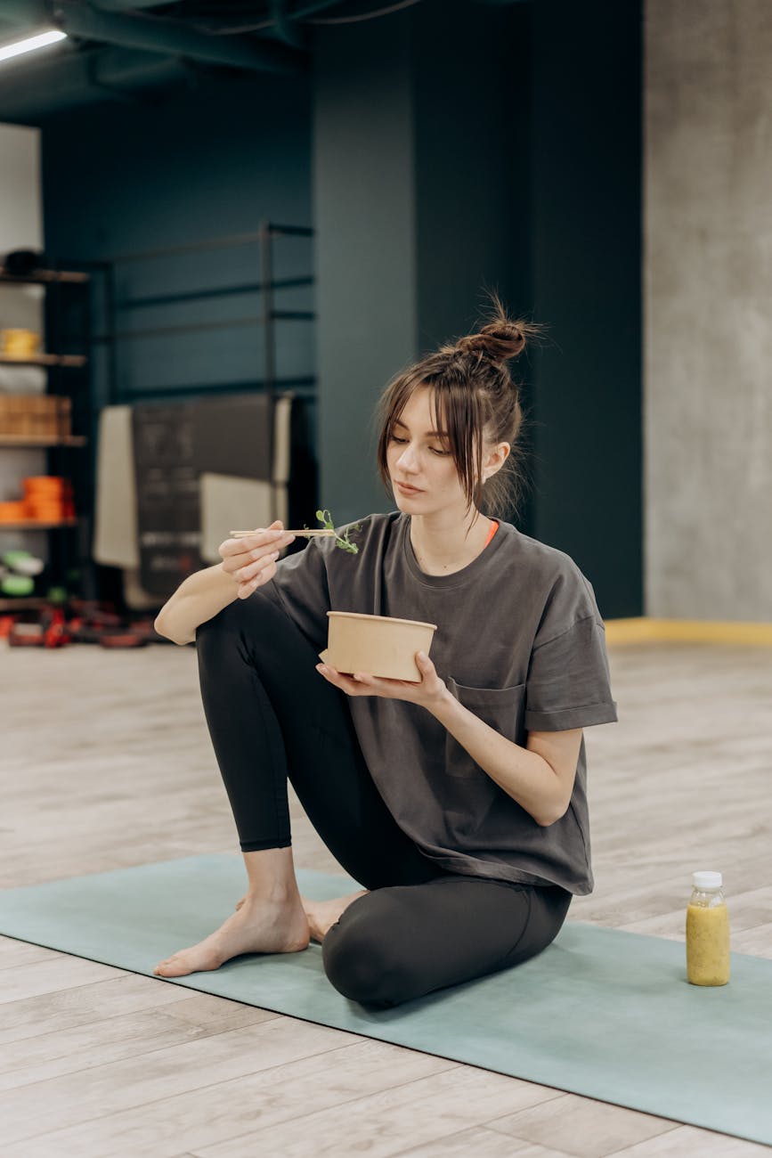 woman in gray t shirt and black leggings sitting on blue yoga mat