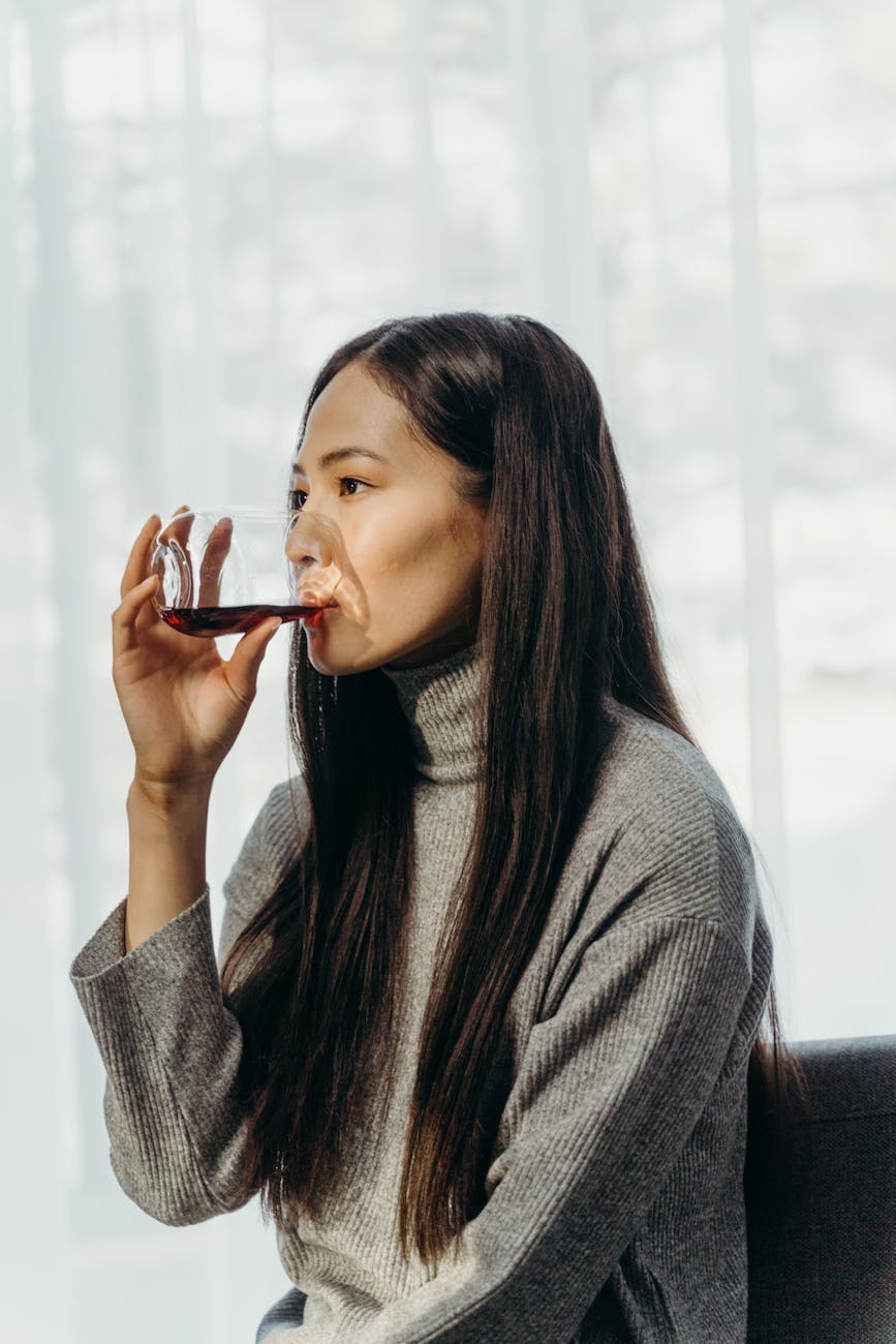 woman in gray sweater drinking from a glass