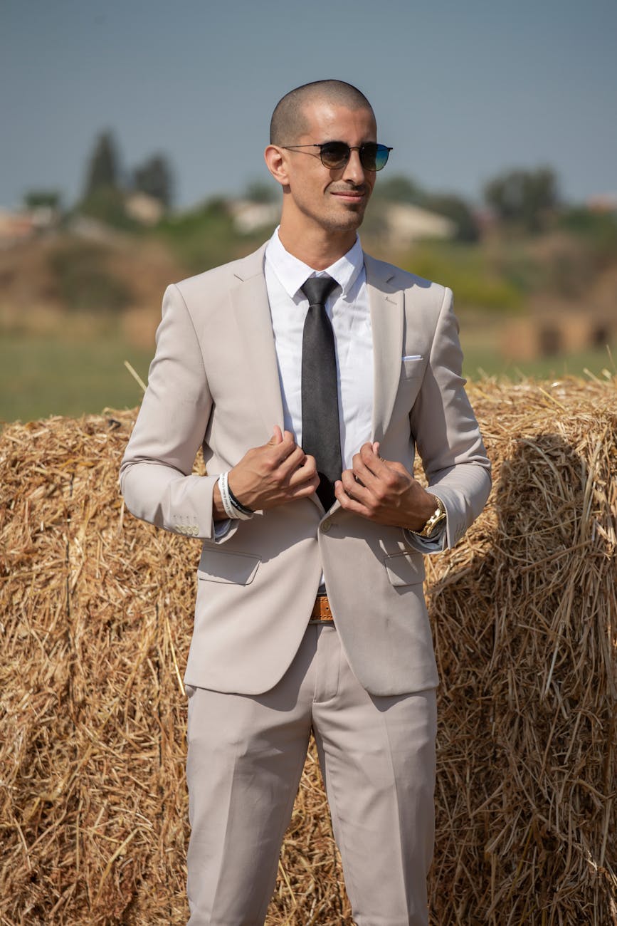 a man in a suit and tie standing in front of hay bales