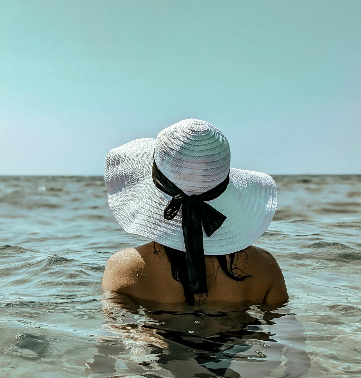 a woman in a white hat is in the ocean