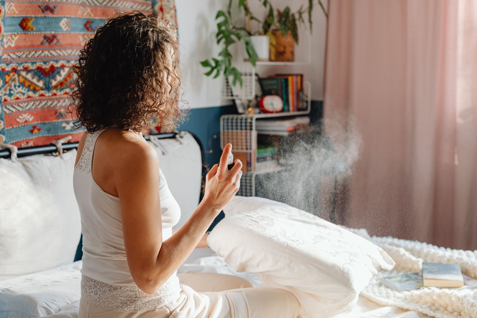 woman sitting on the bed using room spray in her bedroom