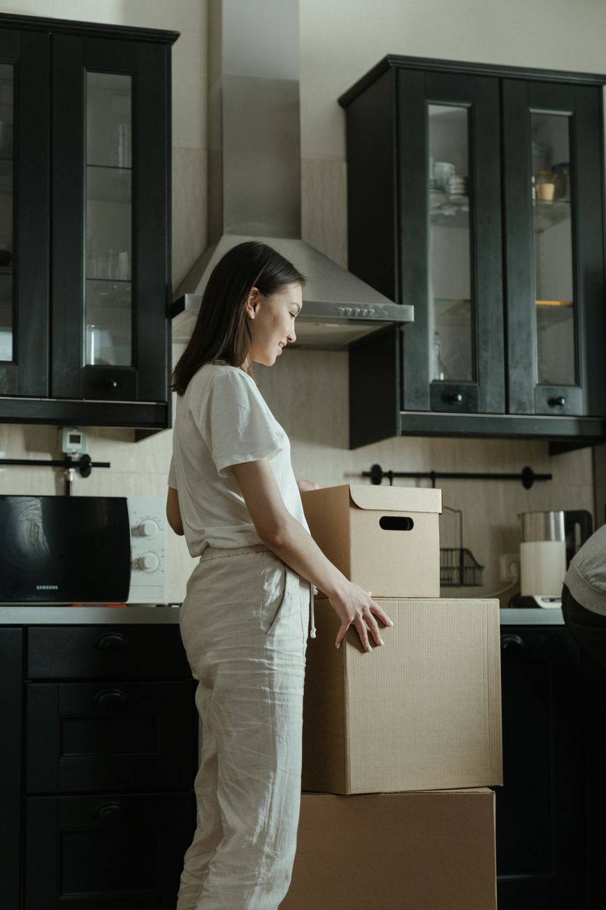 woman in white t shirt and brown pants standing beside kitchen sink