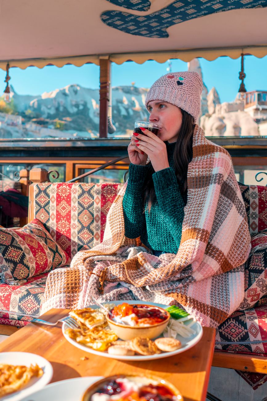 woman wearing winter hat and wrapped in a blanket enjoying meal in a mountain village