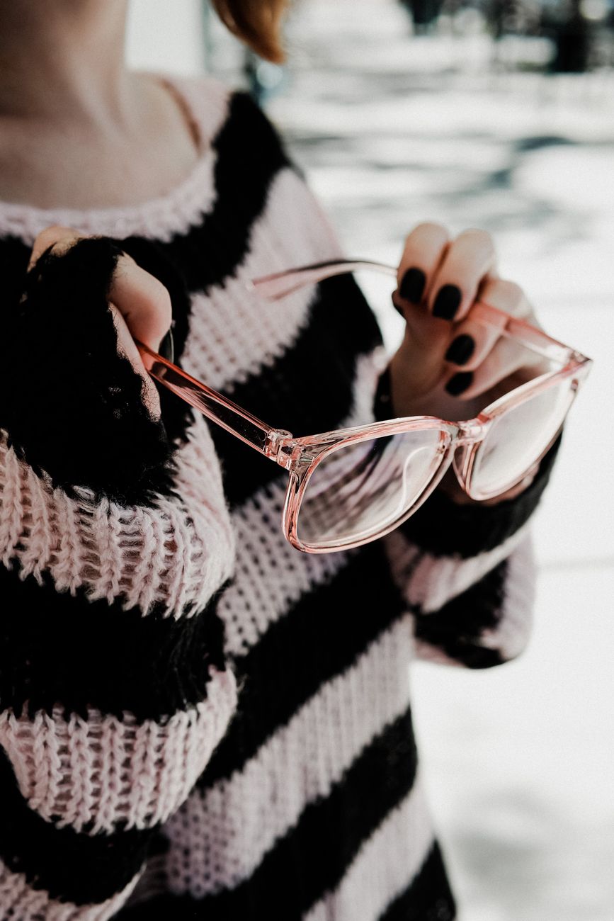 a person wearing striped knitted sweater holding an eyeglasses